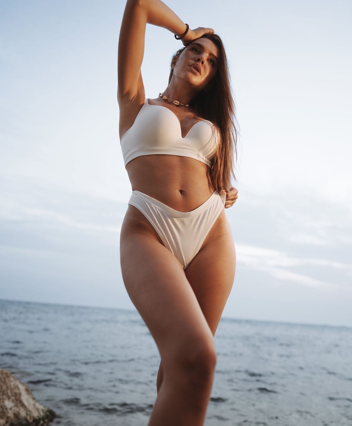 Woman in white bikini by the ocean.