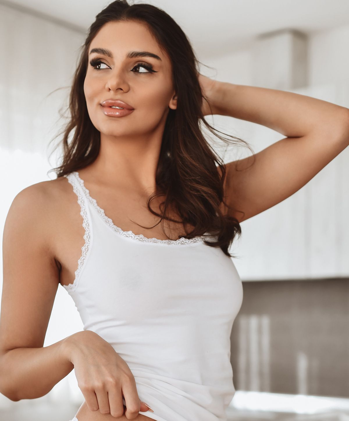 Woman in white tank top with soft smile.