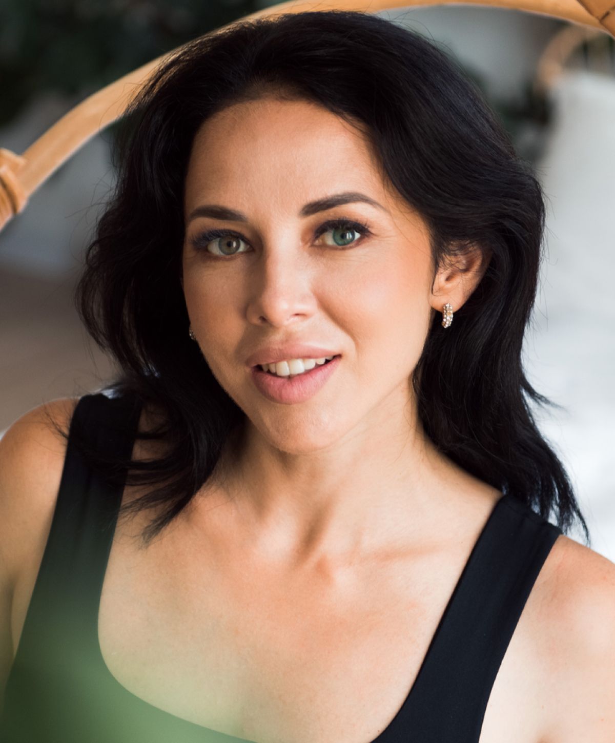 Woman smiling in a casual setting with greenery.