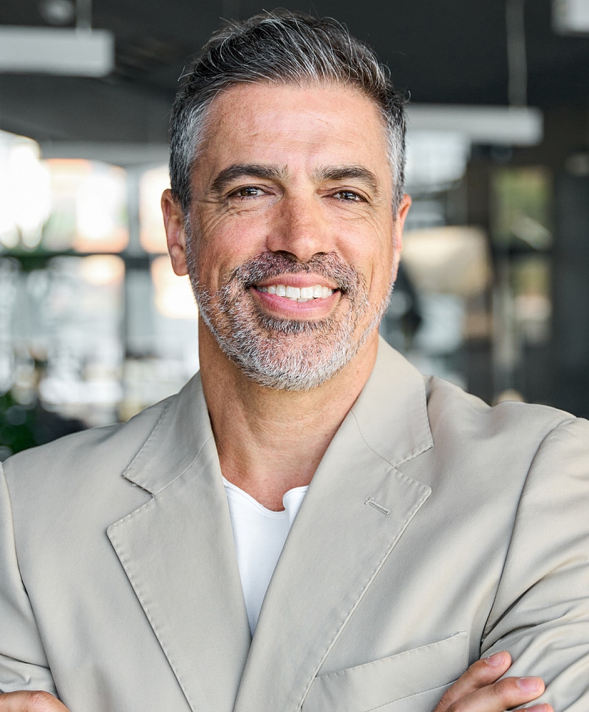 Smiling man in a light jacket, arms crossed.