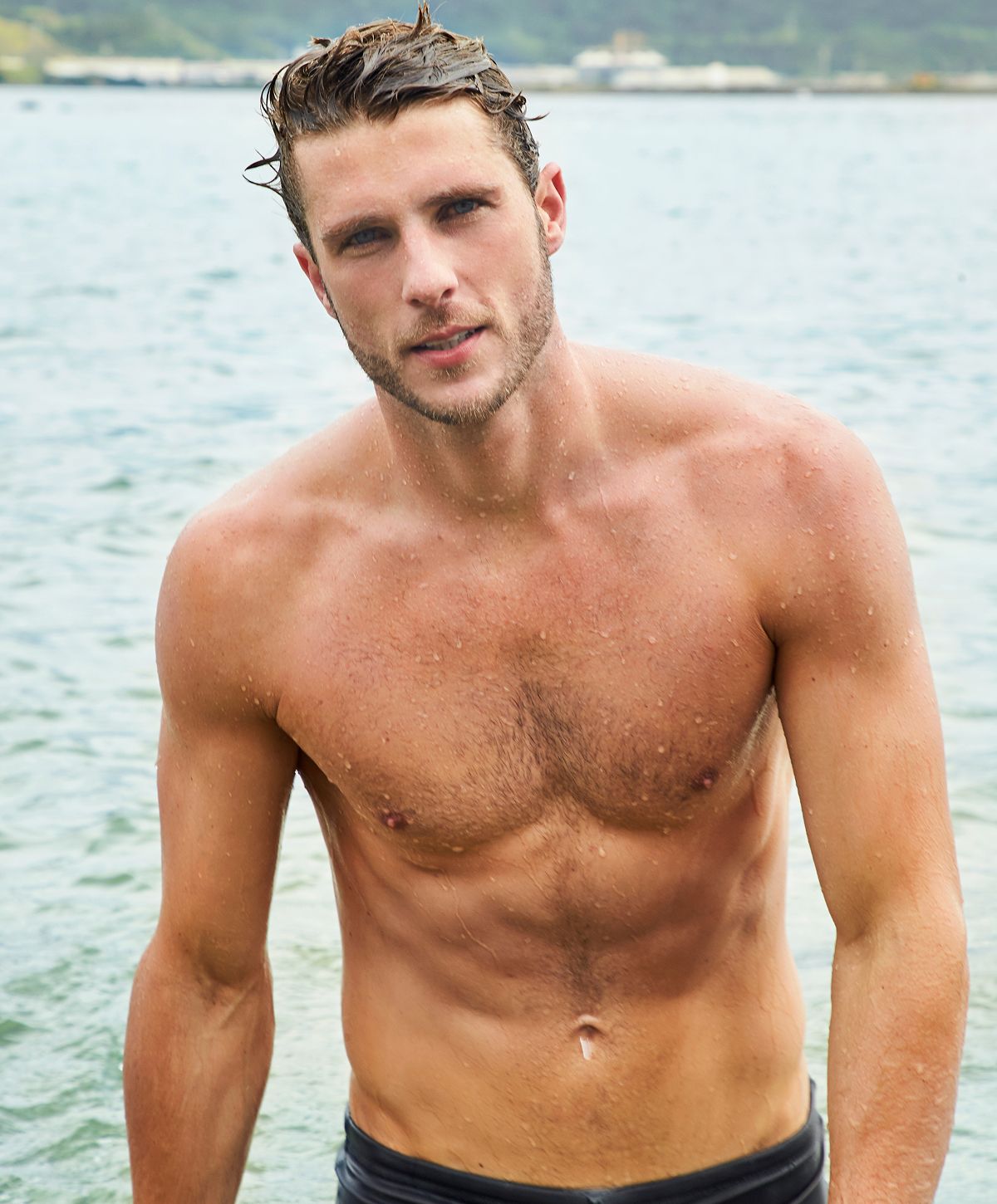 Shirtless man standing in water, relaxed expression.