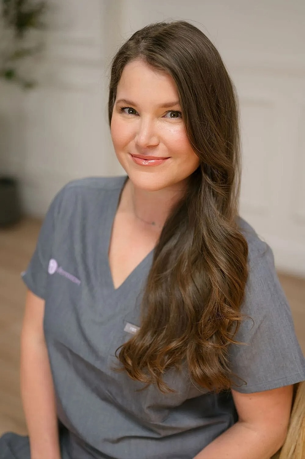 Smiling woman in gray scrubs, professional setting.