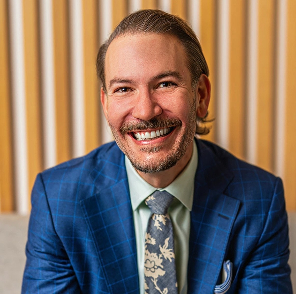 Smiling man in blue suit with patterned tie.
