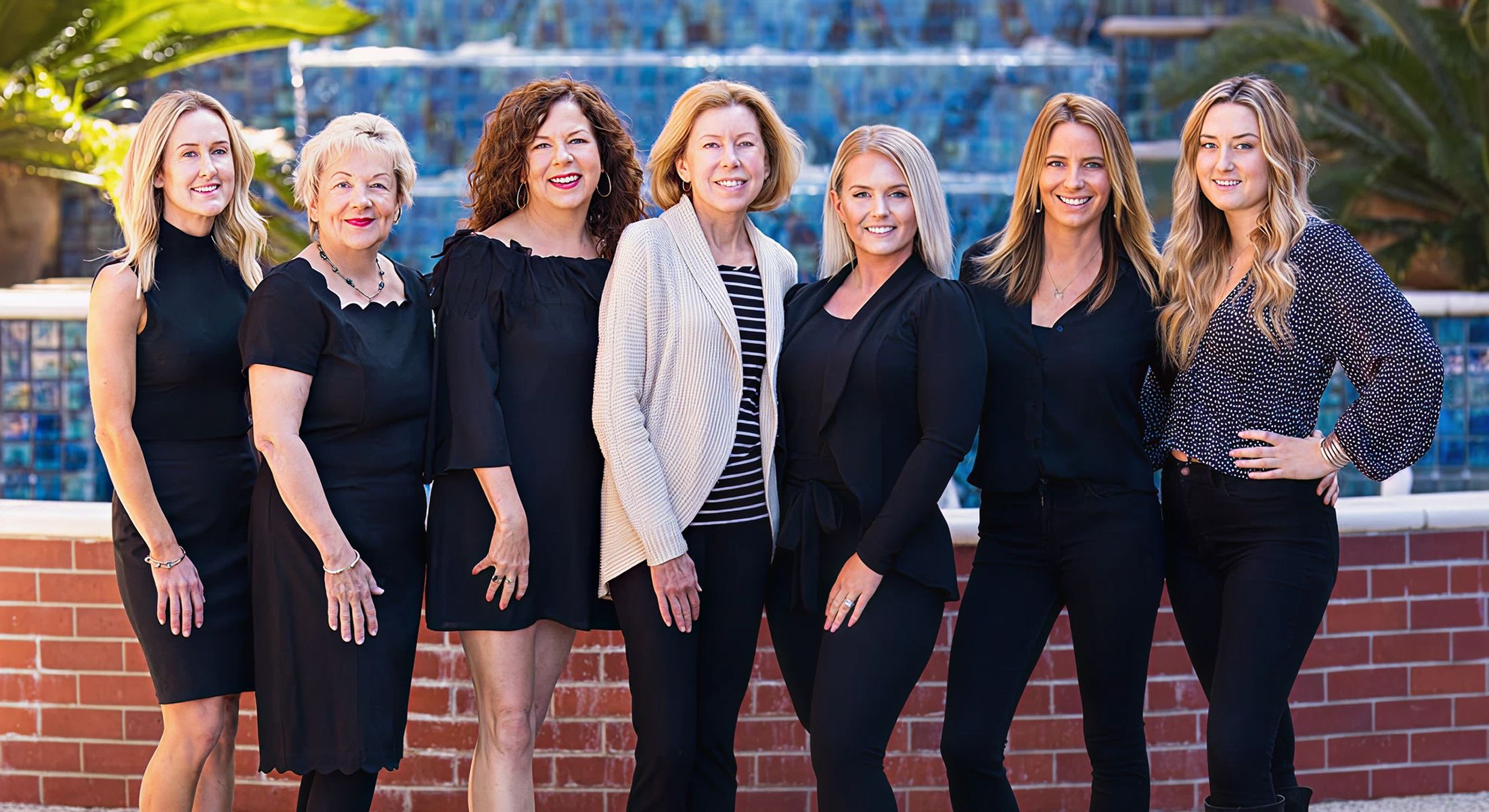 Group of women smiling outdoors in fashionable outfits.