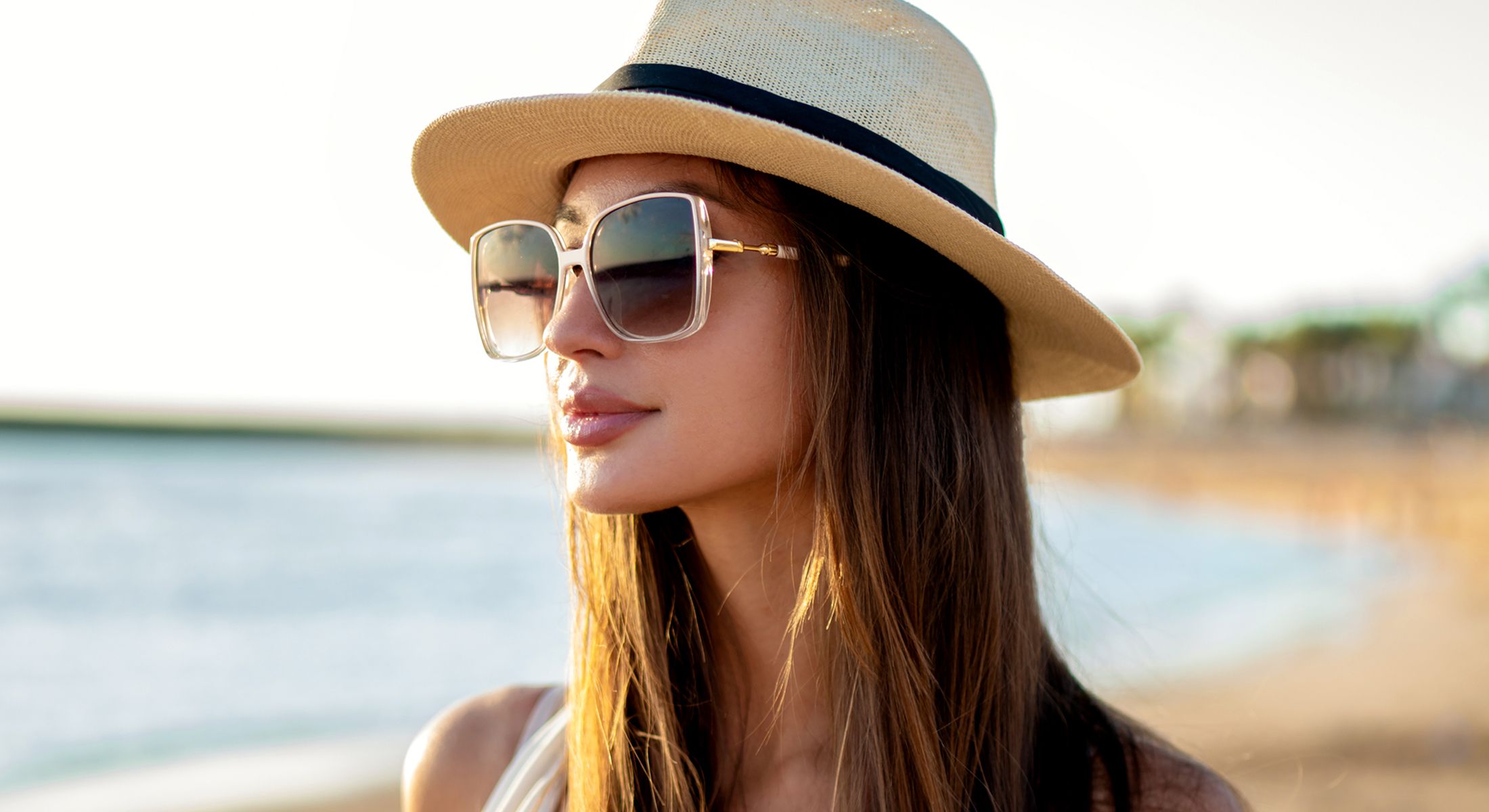 Woman in sunglasses and hat by the beach.