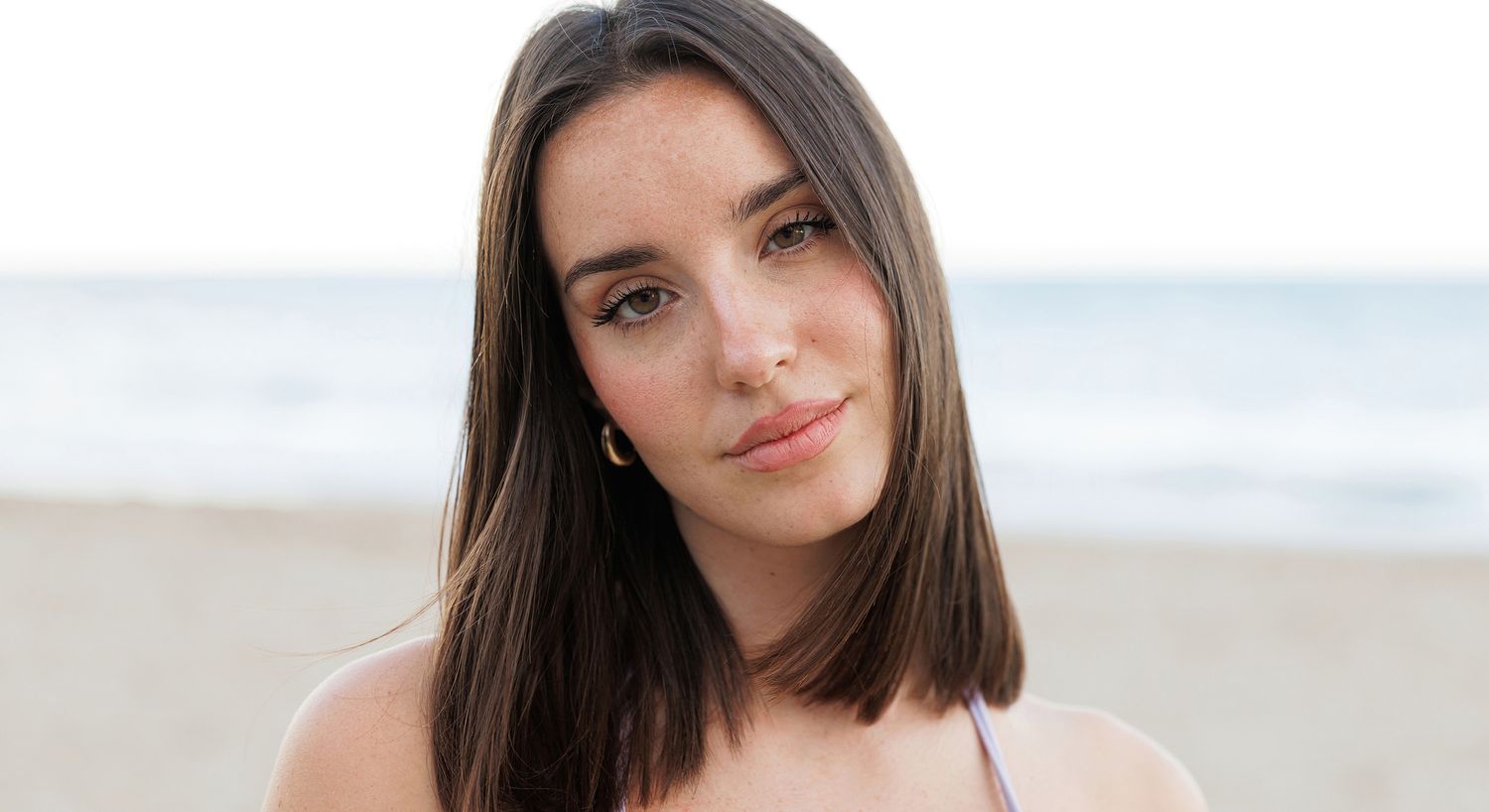 Woman smiling at beach with ocean background.